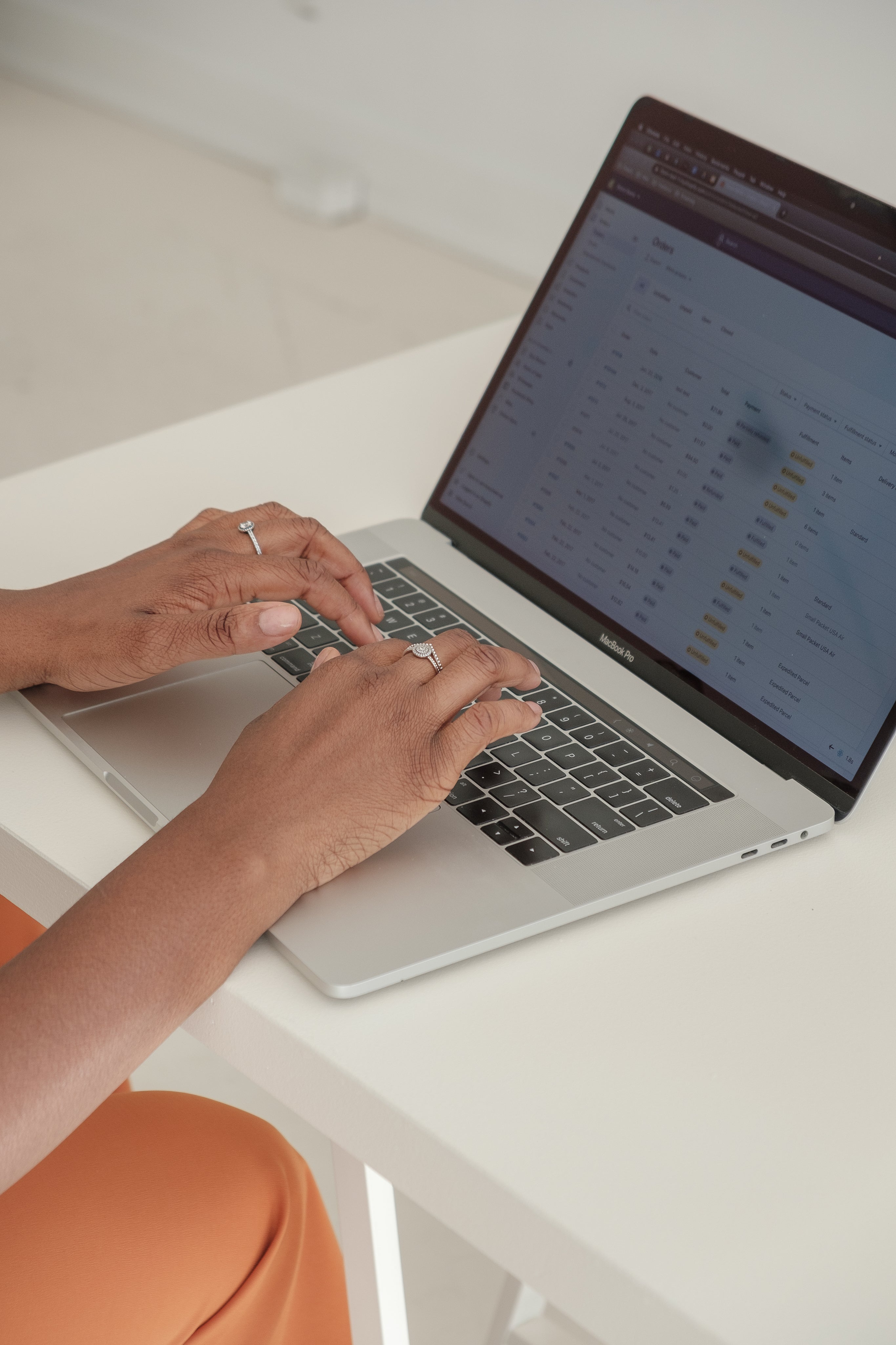 A pair of women's hands typing on a laptop sitting on a white desk. She is logged into the backend of an online store.