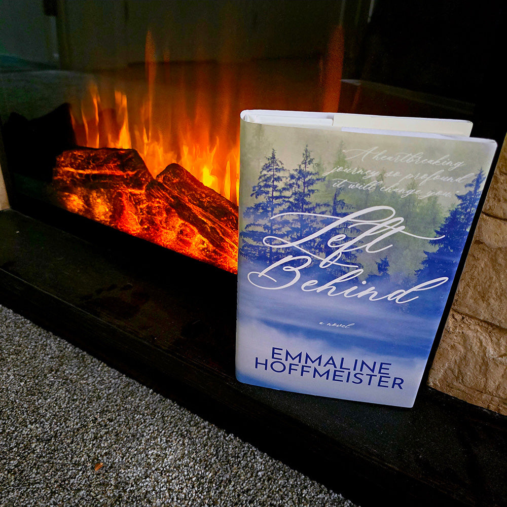 Book titled 'Left Behind' by Emmaline Hoffmeister in front of a fireplace