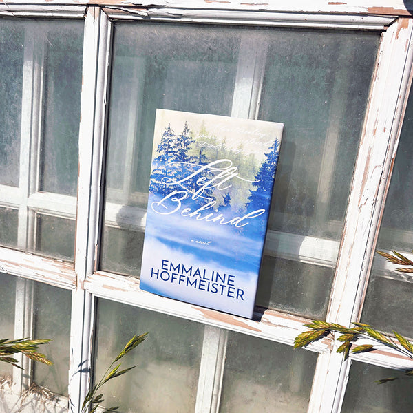 Book titled 'Left Behind' by Emmaline Hoffmeister on a window sill with a scenic cover.