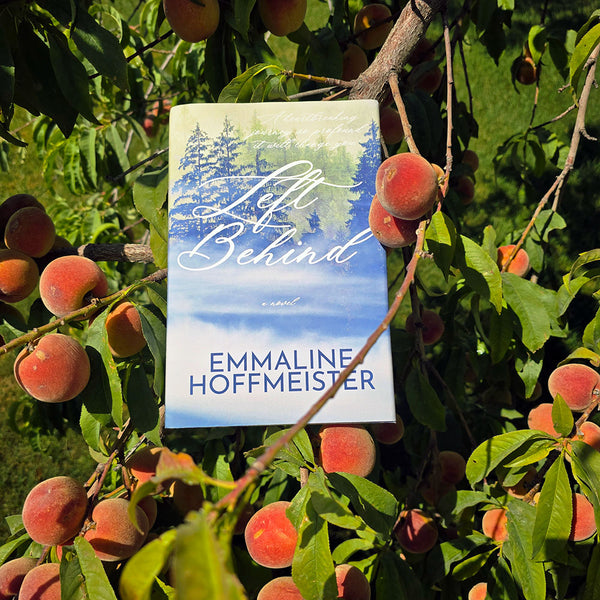 Book titled 'Left Behind' by Emmaline Hoffmeister surrounded by peaches on a tree.